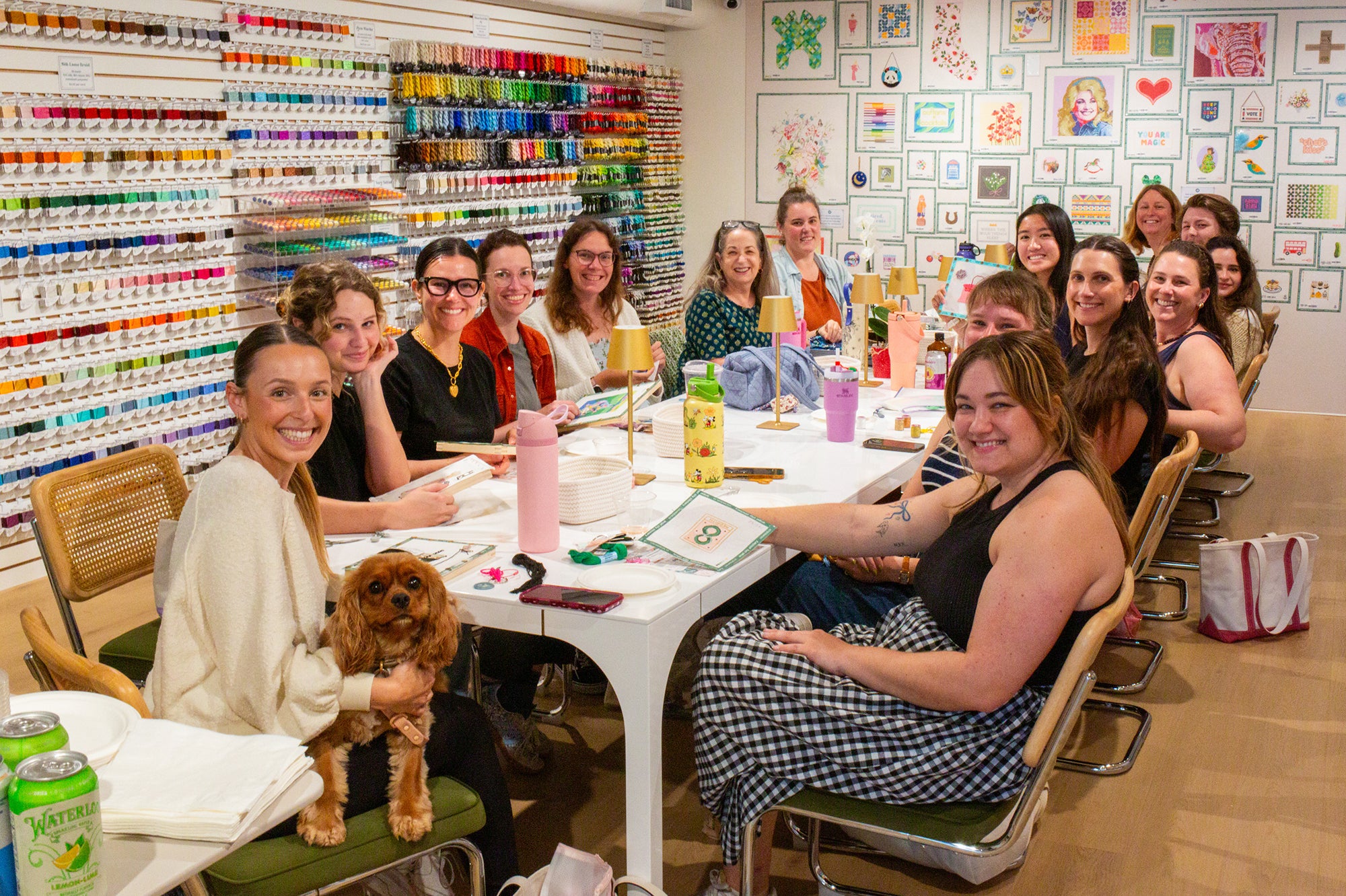 Group of people and a dog sitting around a table in a room with art supplies and artwork on the walls.