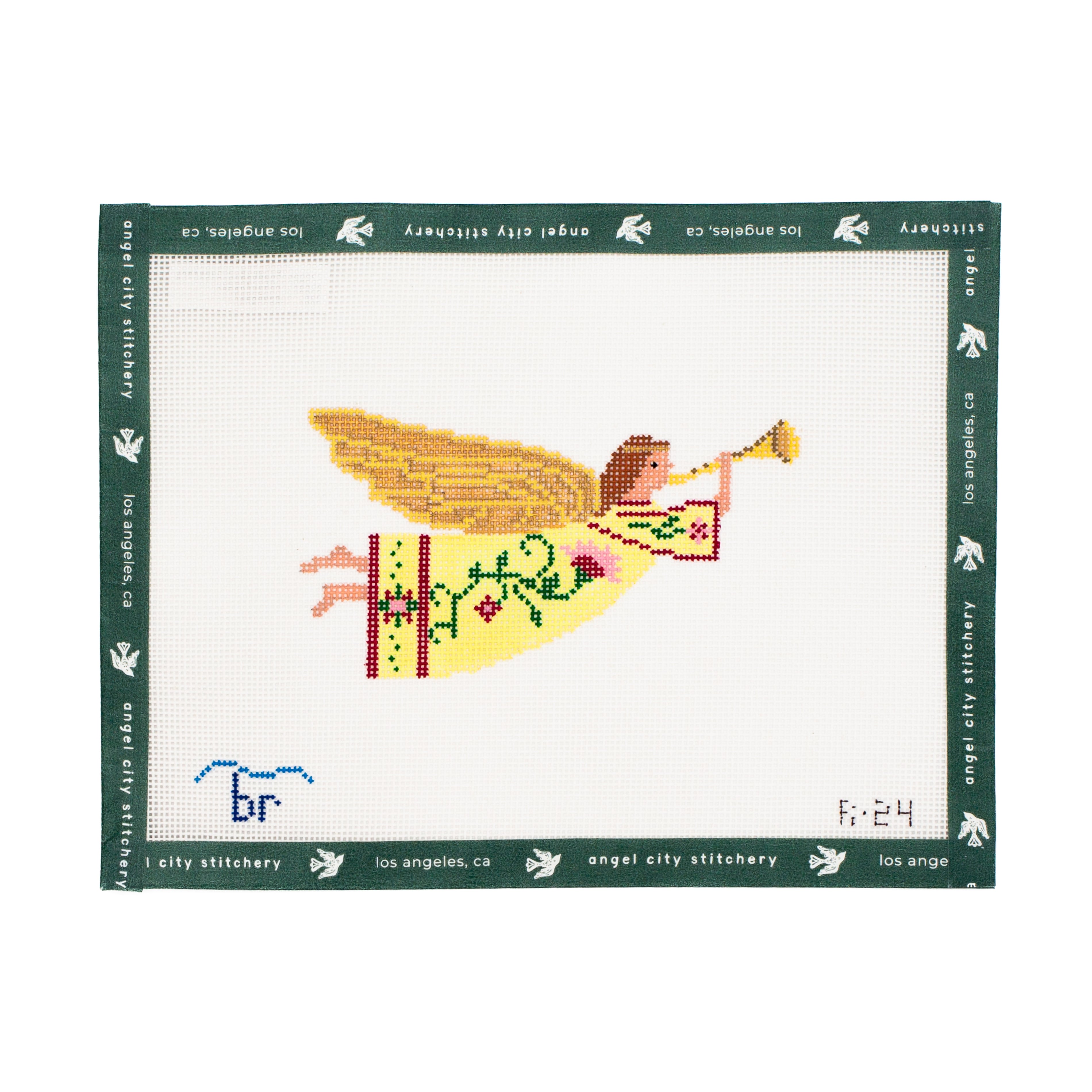 Cross-stitched angel with a trumpet needlepoint canvas with green border, featuring 'Angel City Stitchery' branding.