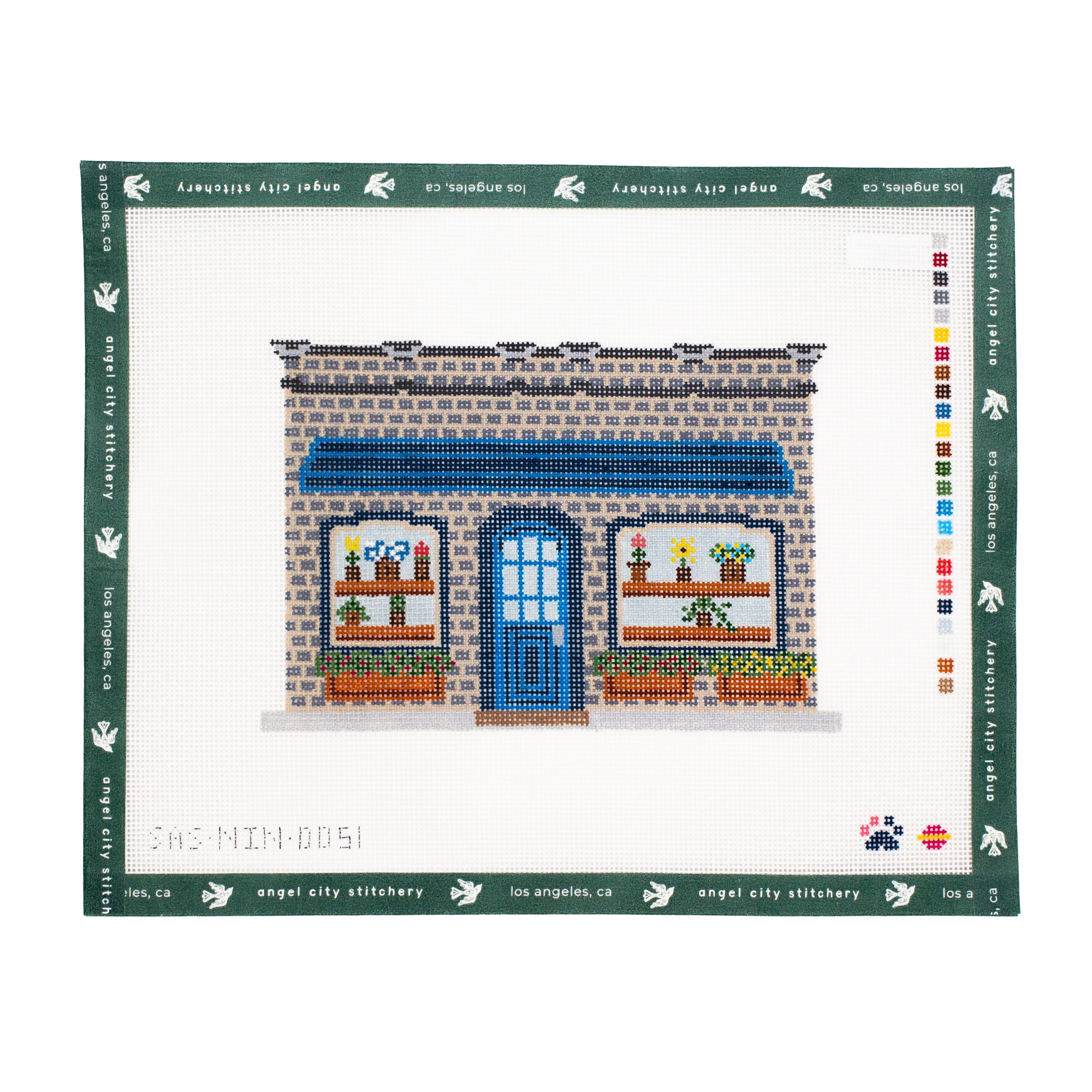Needlepoint canvas of a brick home with flowers in the windows and blue door on a white background.