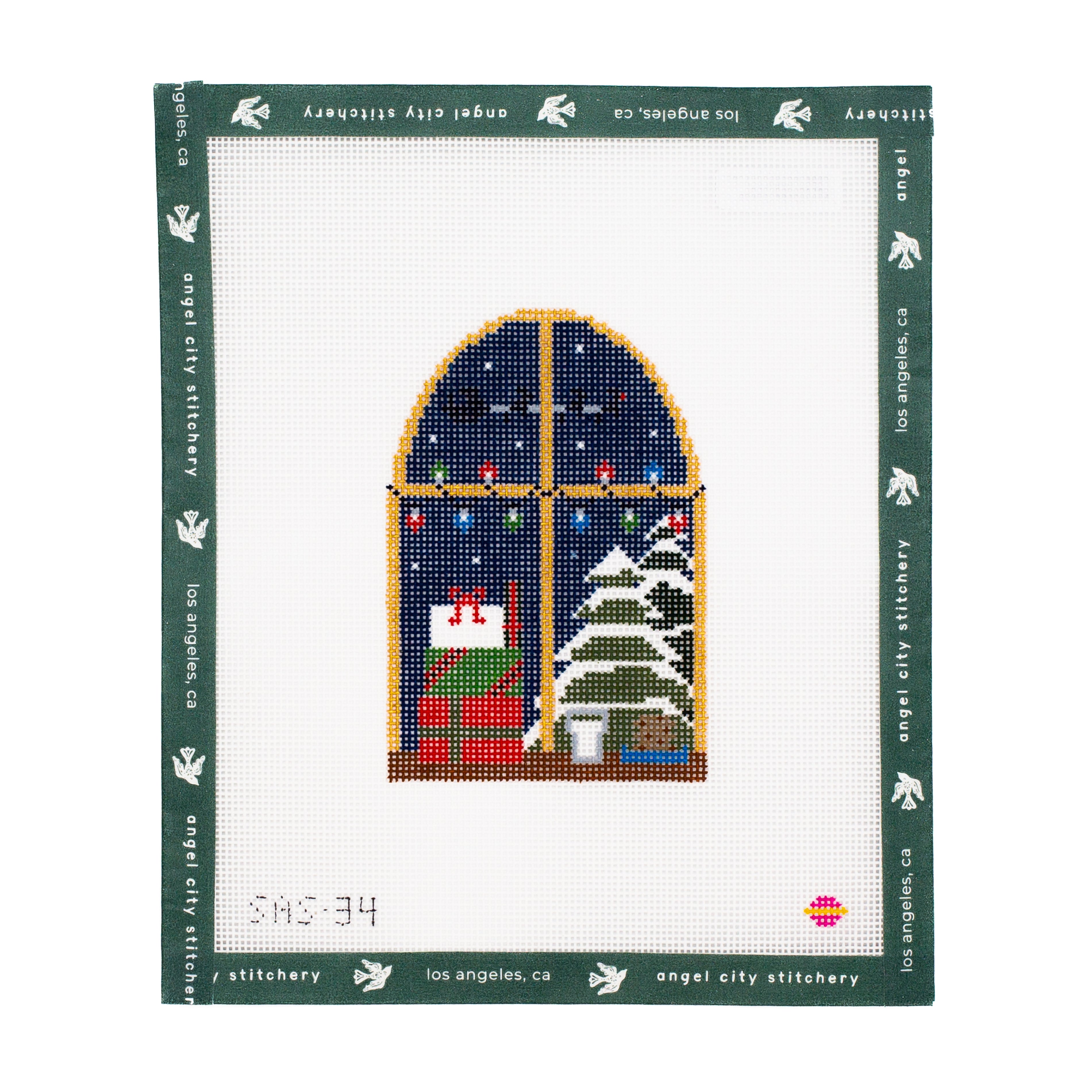 Needlepoint canvas  with a Christmas scene of a house and tree, framed by Angel City Stitchery.