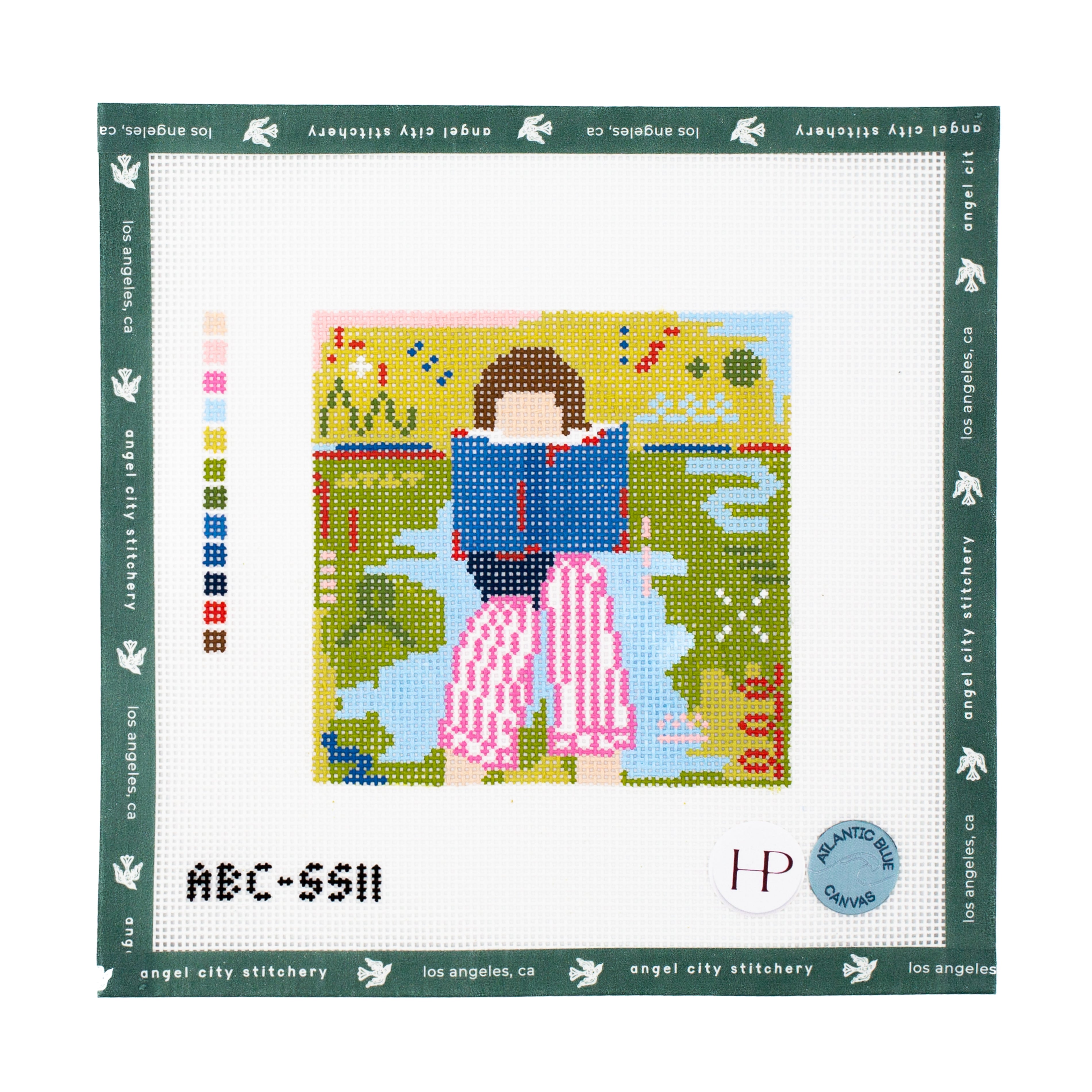 Needlepoint canvas with pattern of a person sitting on a bench with a book, surrounded by nature, with 'Angel City Stitchery' branding.
