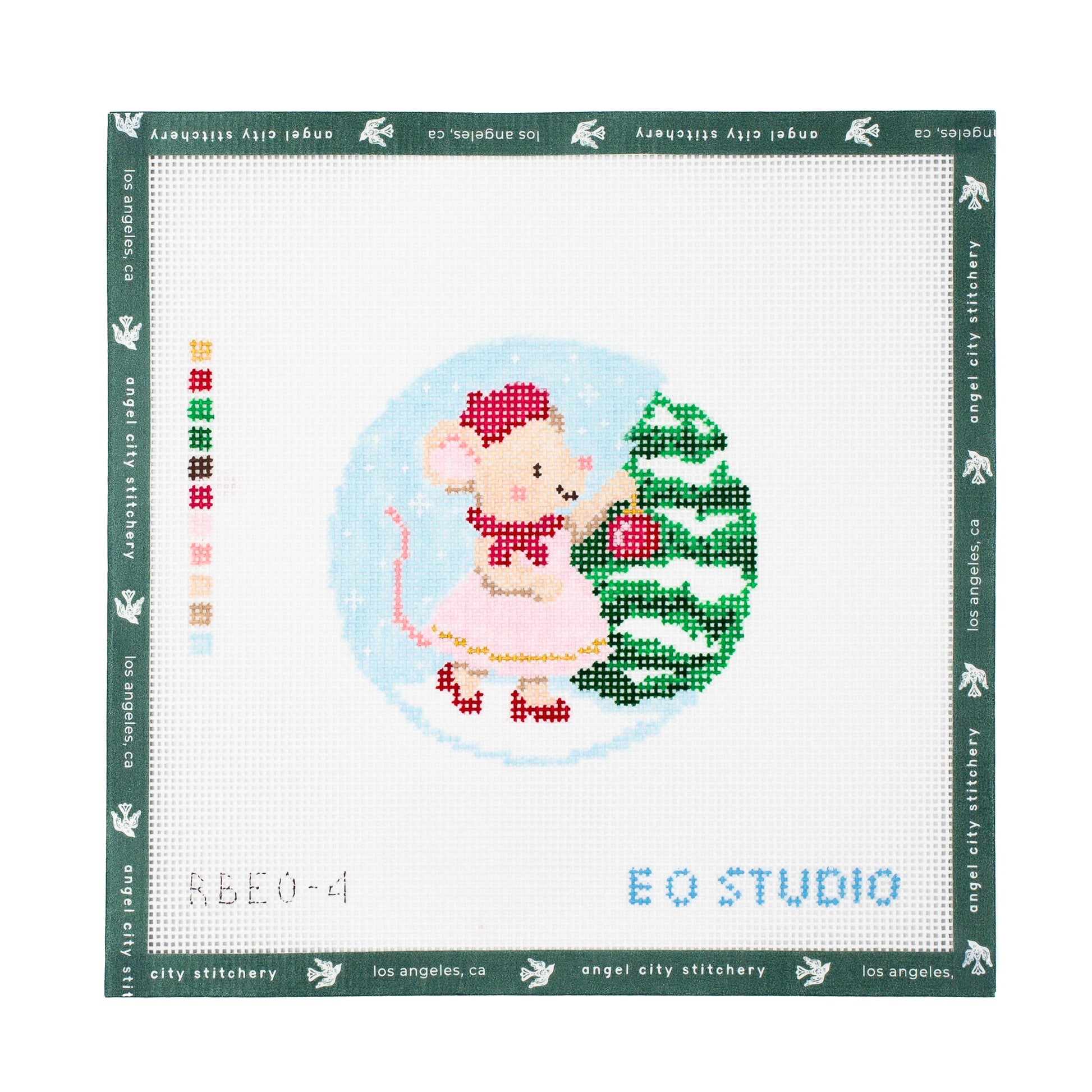 A square needlepoint canvas from EO Studio by Angel City Stitchery, featuring a pixelated mouse in a pink dress next to a green Christmas tree inside a light blue circle.