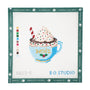 Christmas-themed hot cocoa or coffee mug needlepoint canvas featuring a light blue mug with the word "NOËL" in yellow, a holly motif, whipped cream topped with colorful sprinkles, chocolate drizzle, and a candy cane straw on a white background