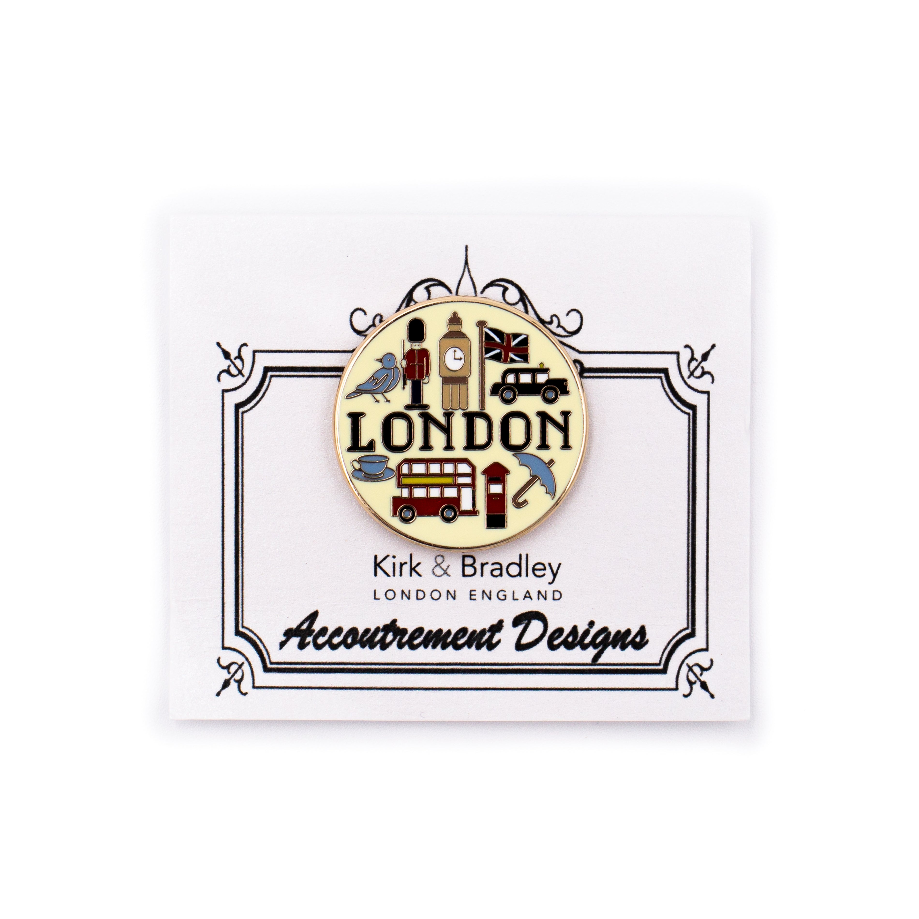 A round enamel pin by Kirk & Bradley featuring London-themed icons including Big Ben, a double-decker bus, a telephone box, and the word "LONDON", mounted on a white display card with decorative borders