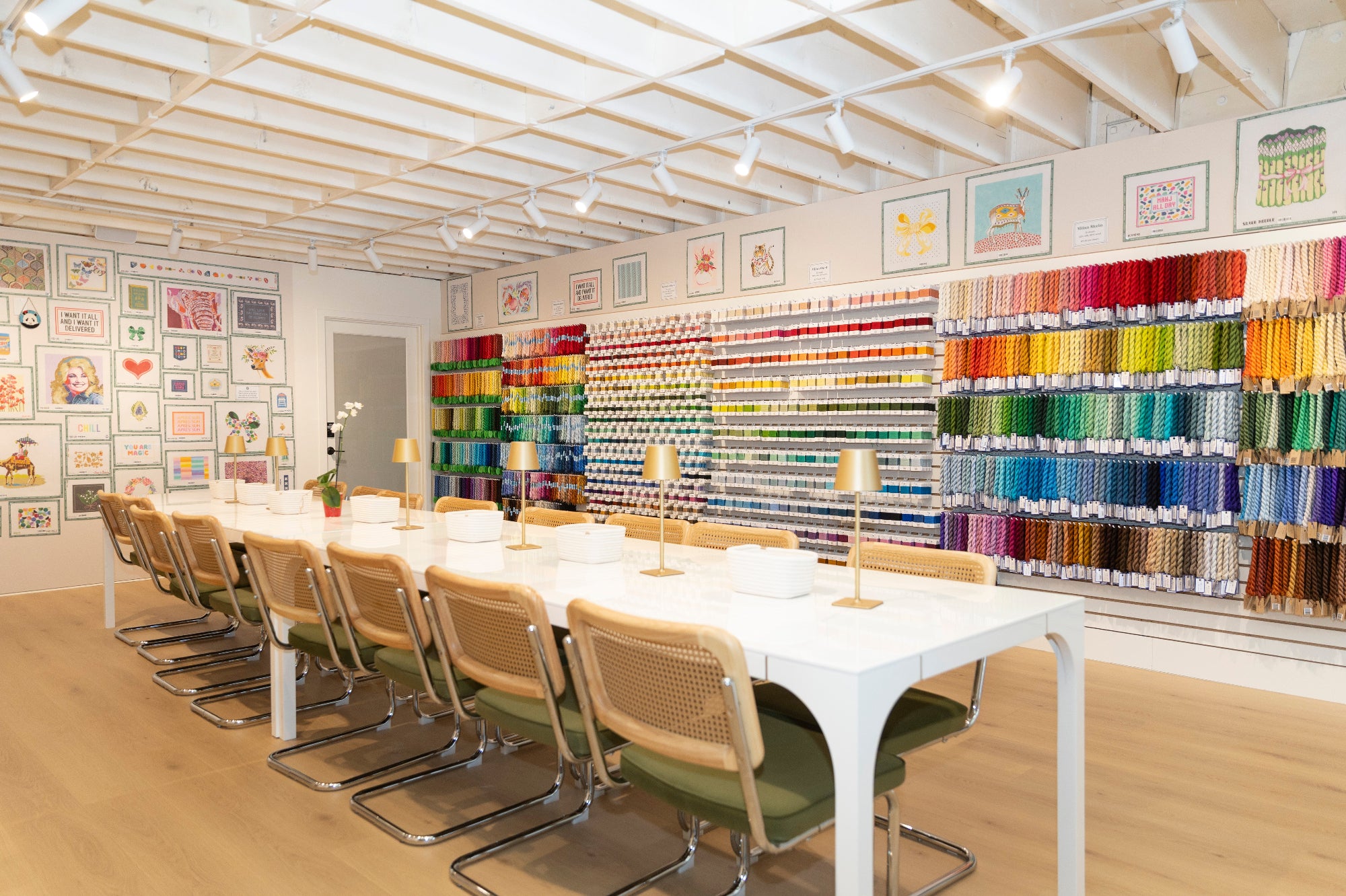 Colorful yarn display with a long table and chairs in a room with white walls and wooden floor.