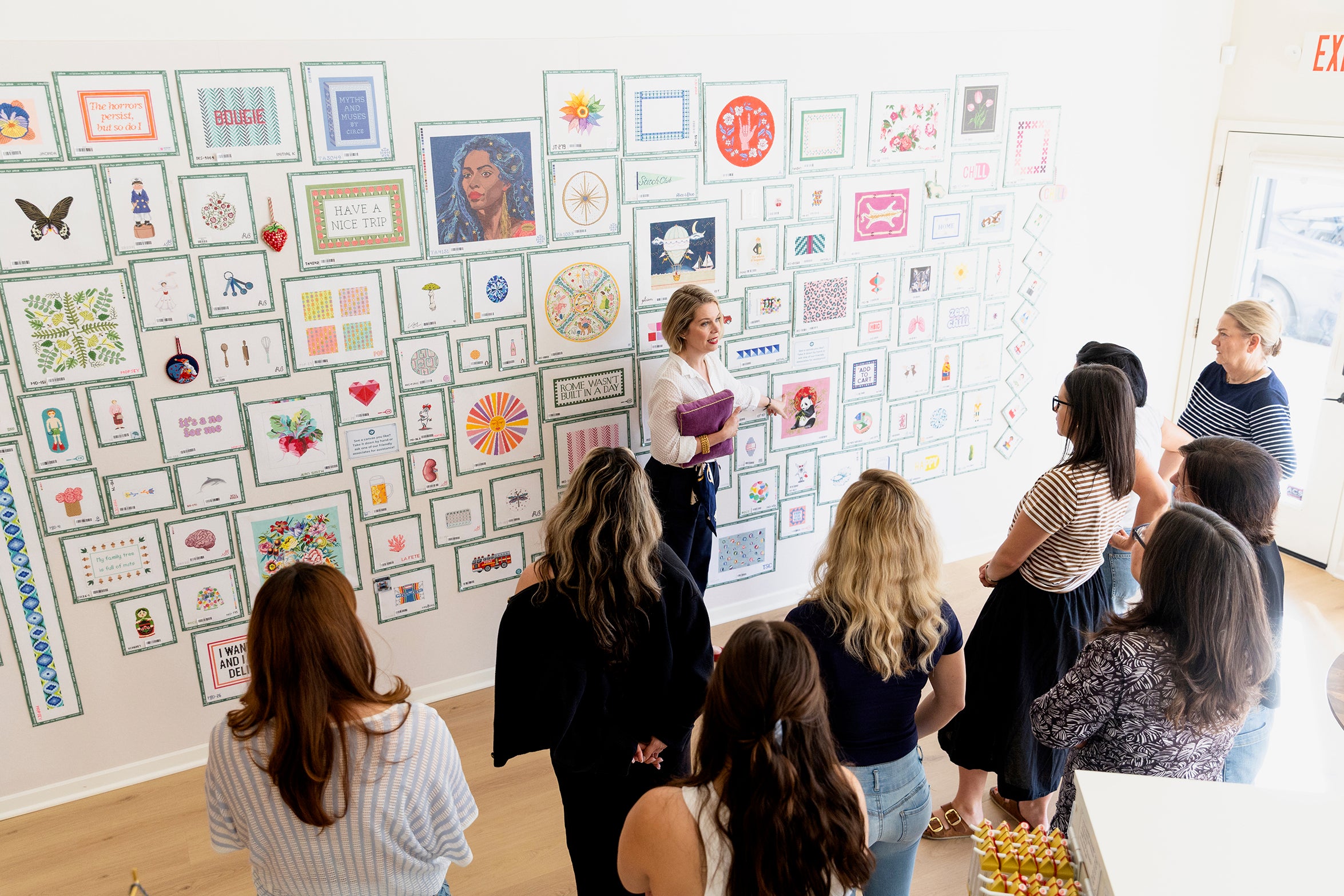 Group of people observing a wall with various framed artworks in an indoor setting.