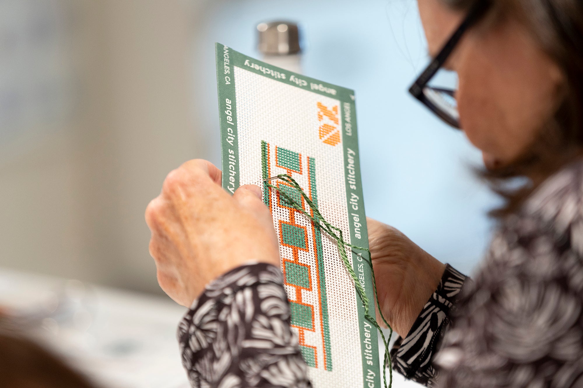 Person holding a cross-stitch pattern with a blurred background