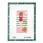 A finished needlepoint canvas featuring a woman in a red swimsuit lying on a pink and green striped beach towel with a hat, sunglasses, and a basket, bordered by a green brand frame. The text 'NTG-KB098' and 'angel city stitchery' are visible at the bottom.