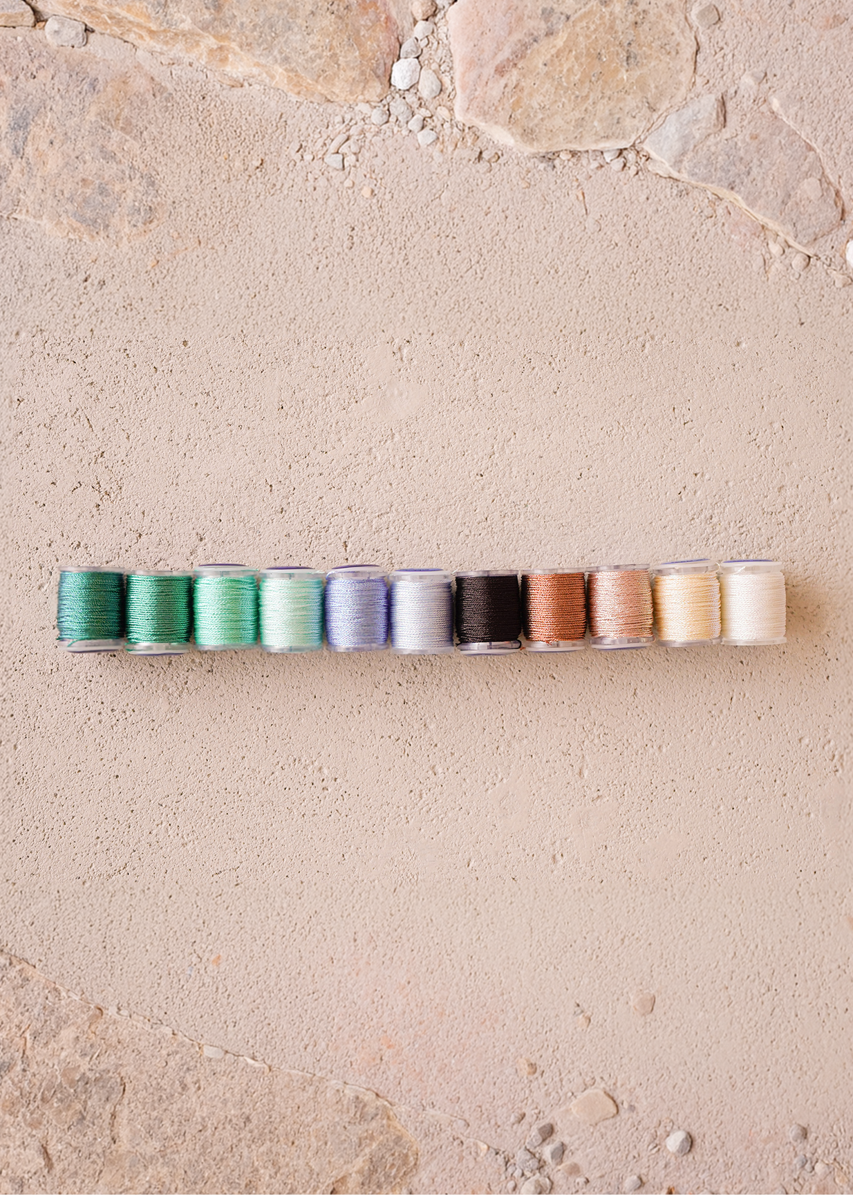 Row of spools of thread in various colors on a stone surface